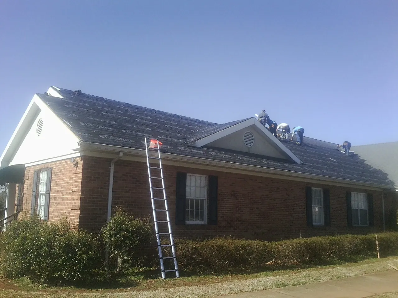 Crew tearing shingles off a brick ranch roof with a ladder set — Emergency Roof Repair work by our crew in Mansfield Center