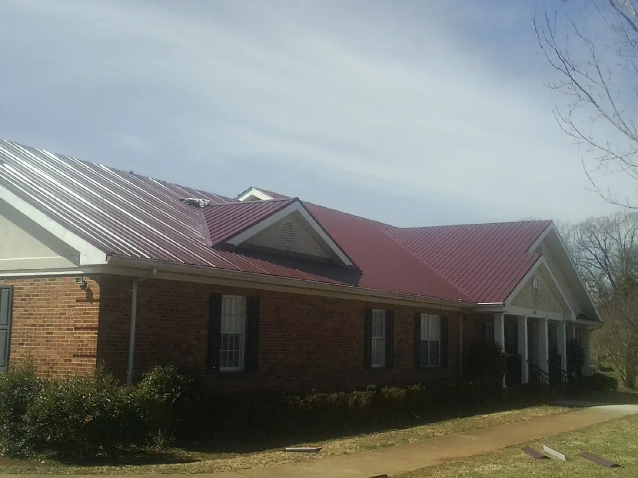 Red metal roof with gabled entries on a long brick building, from a Hail Damage Roof Repair job in Mansfield Center