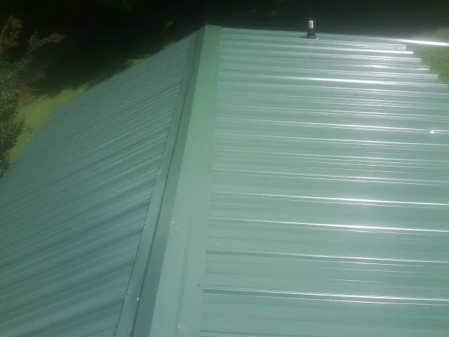 New green metal panels meeting at the ridge of a roof — Flat Roof Repair work by our crew in Mansfield Center
