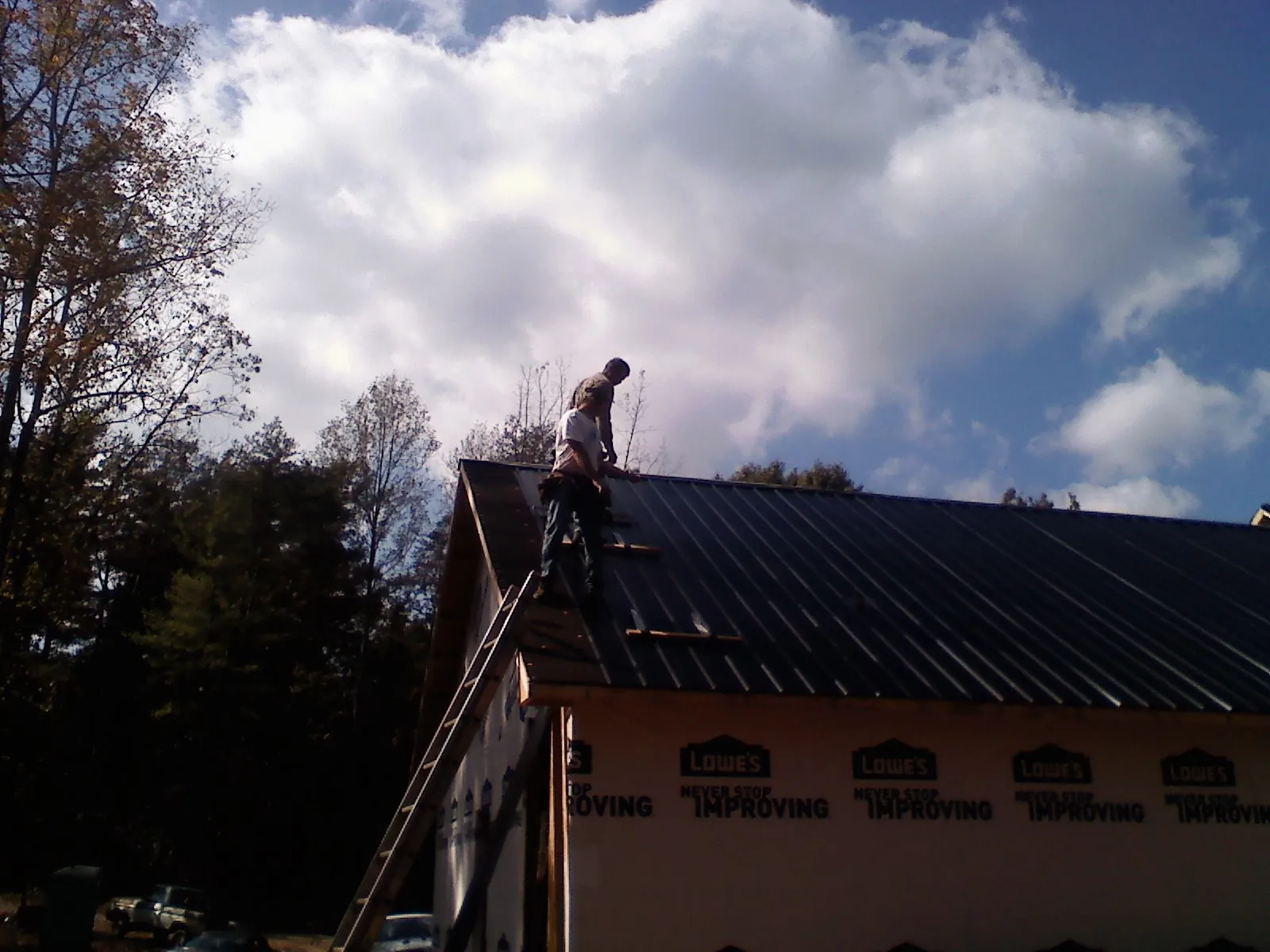 Roofer fastening dark metal panels high against a cloudy sky, from a Roof Inspection job in Mansfield Center