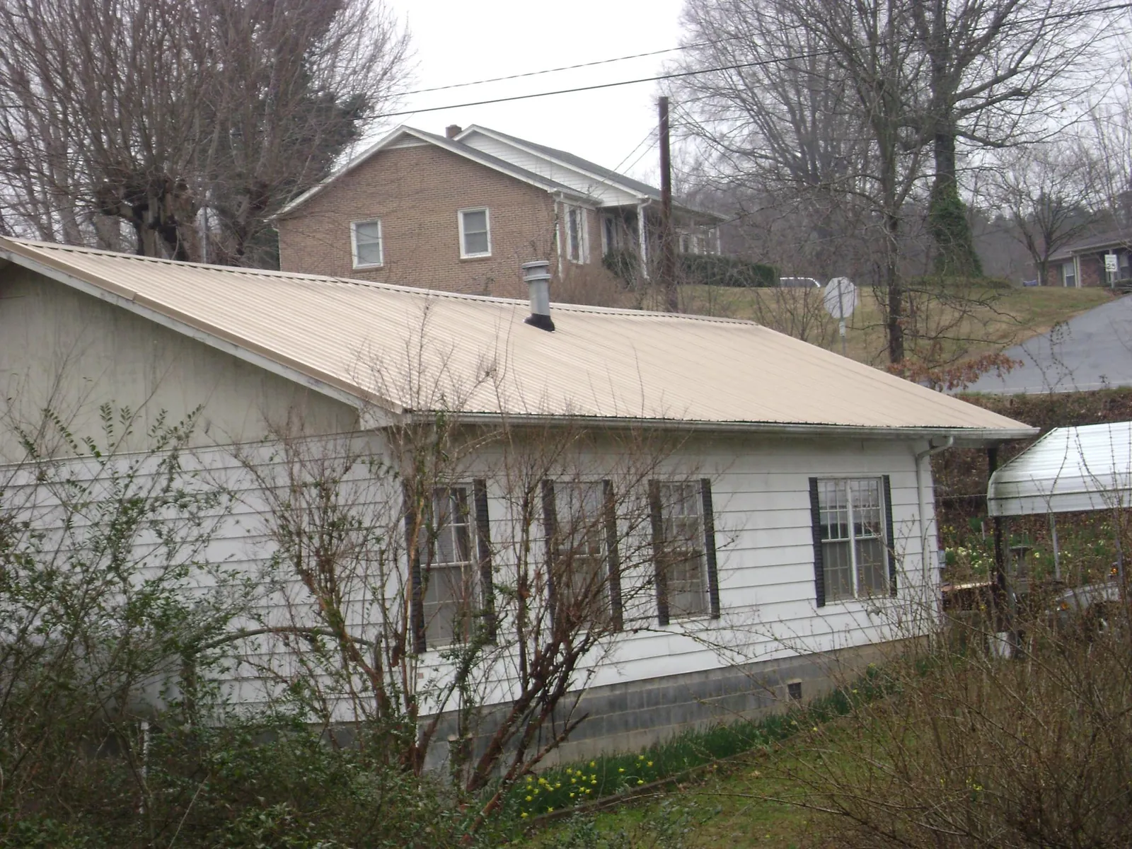 Tan metal roof on a white sided house set into a hillside — Commercial Roofing by Roofing Brothers in Mansfield Center