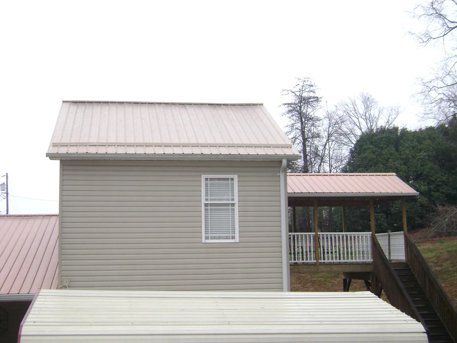 Tan metal roofs on a two story addition and attached porch, from a Roof Replacement job in Mansfield Center